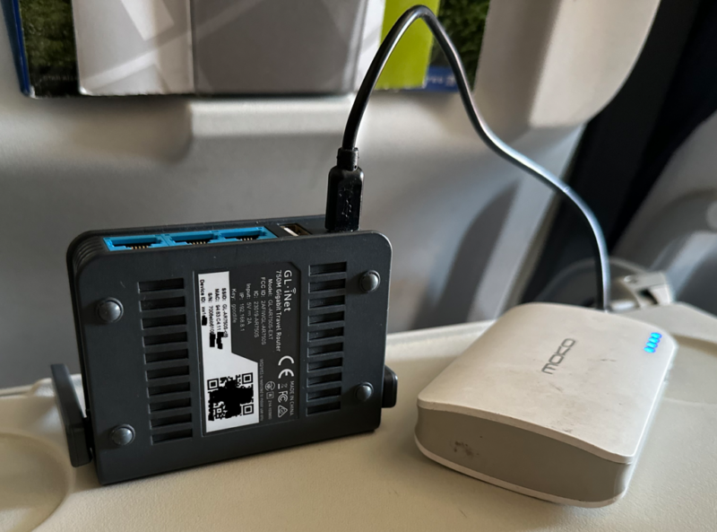 GL.iNet AR750S-EXT sitting on an airplane tray with a small USB battery pack rebroadcasting wi-fi